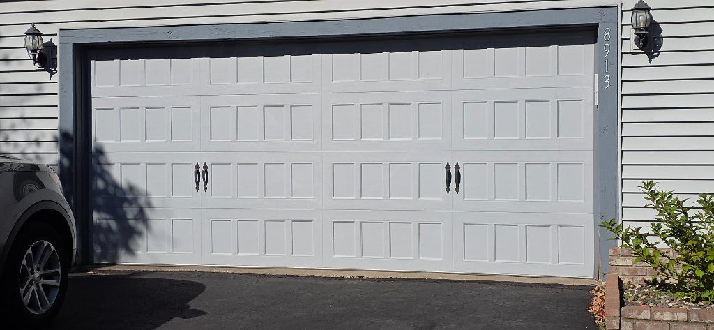 White double garage door on a house with gray siding and a parked car partially visible on the left.