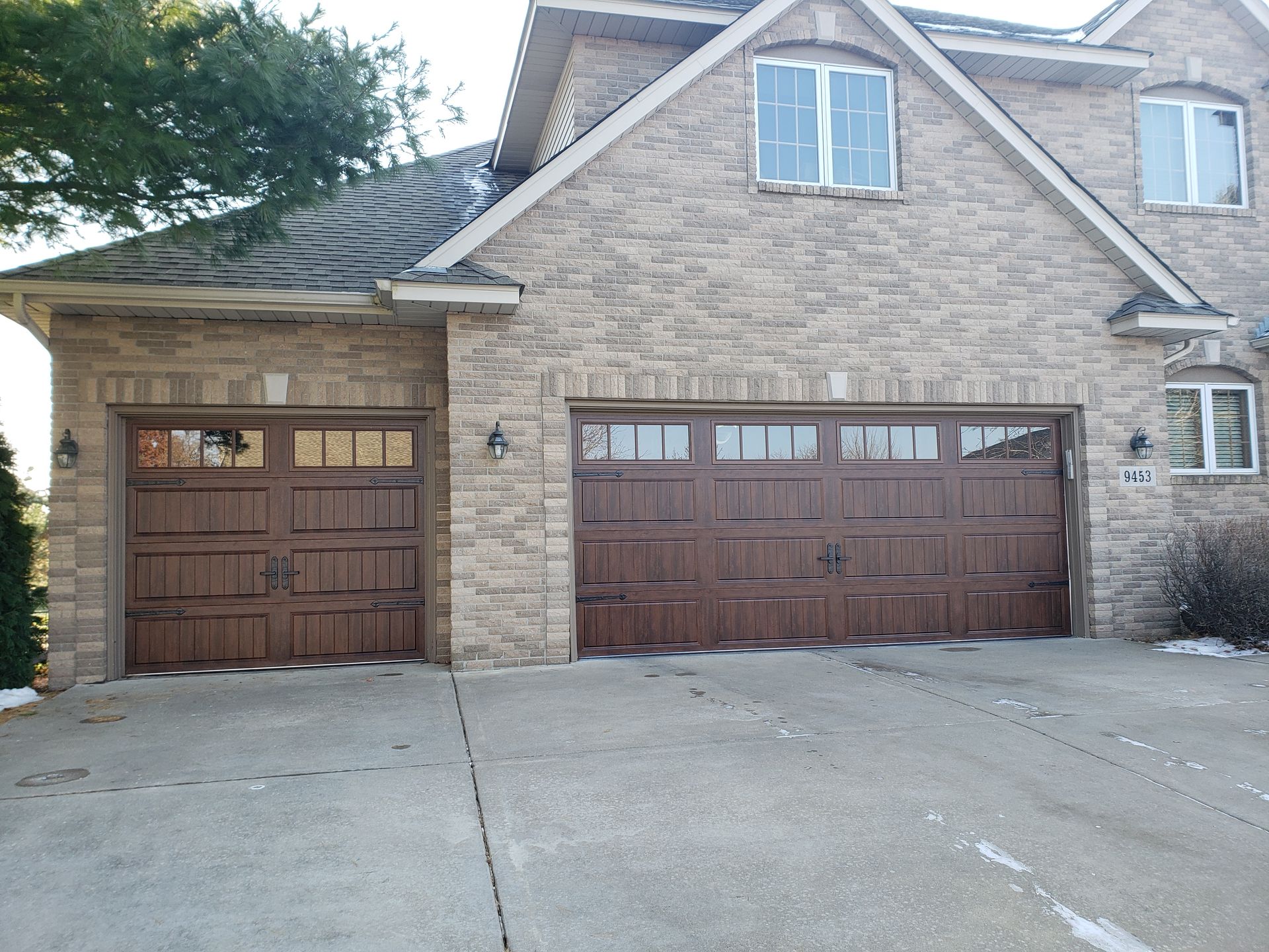 Two brown wooden garage doors on a stone house with a concrete driveway