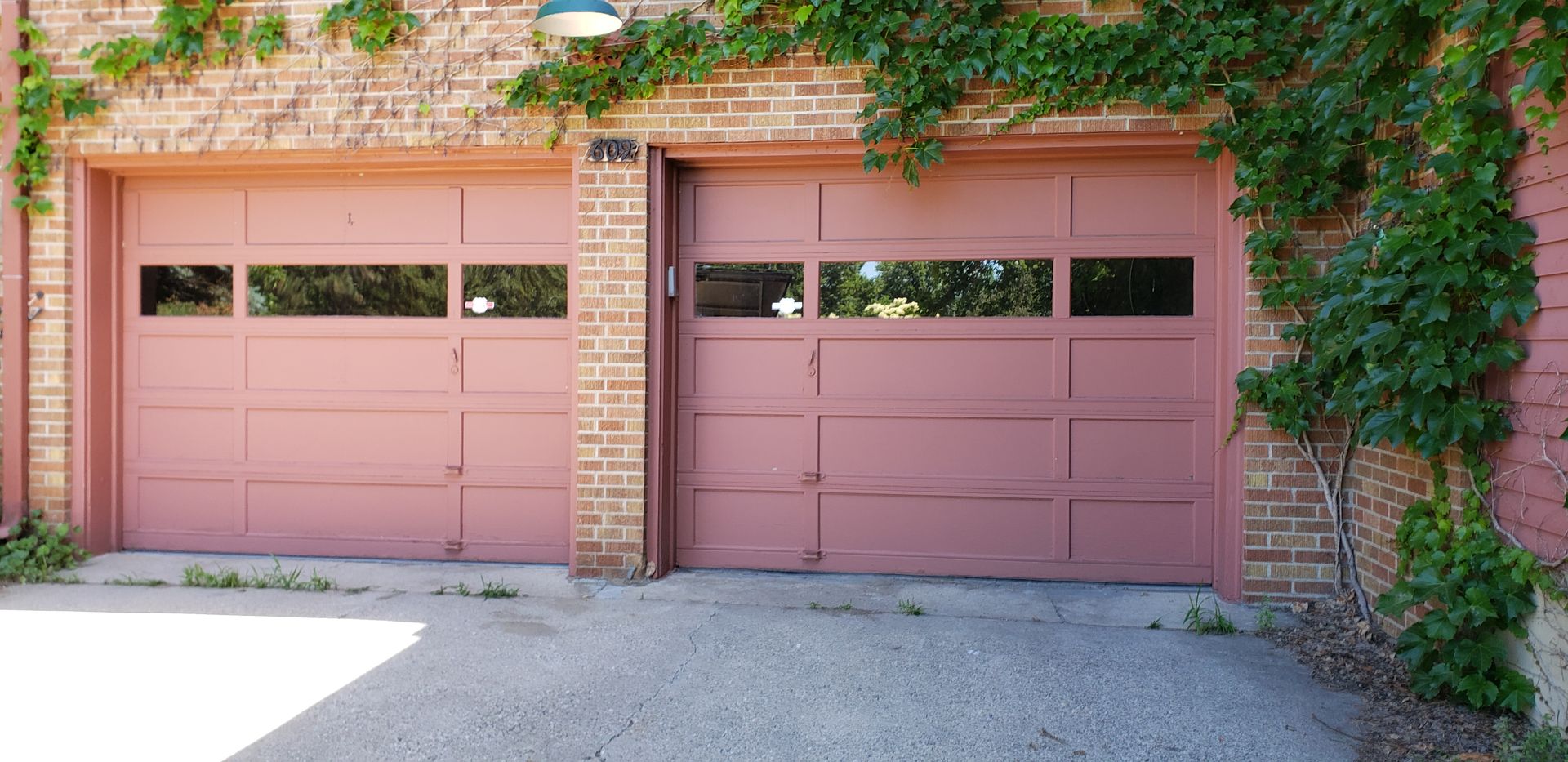 Two pink garage doors on a brick building with ivy and greenery above.