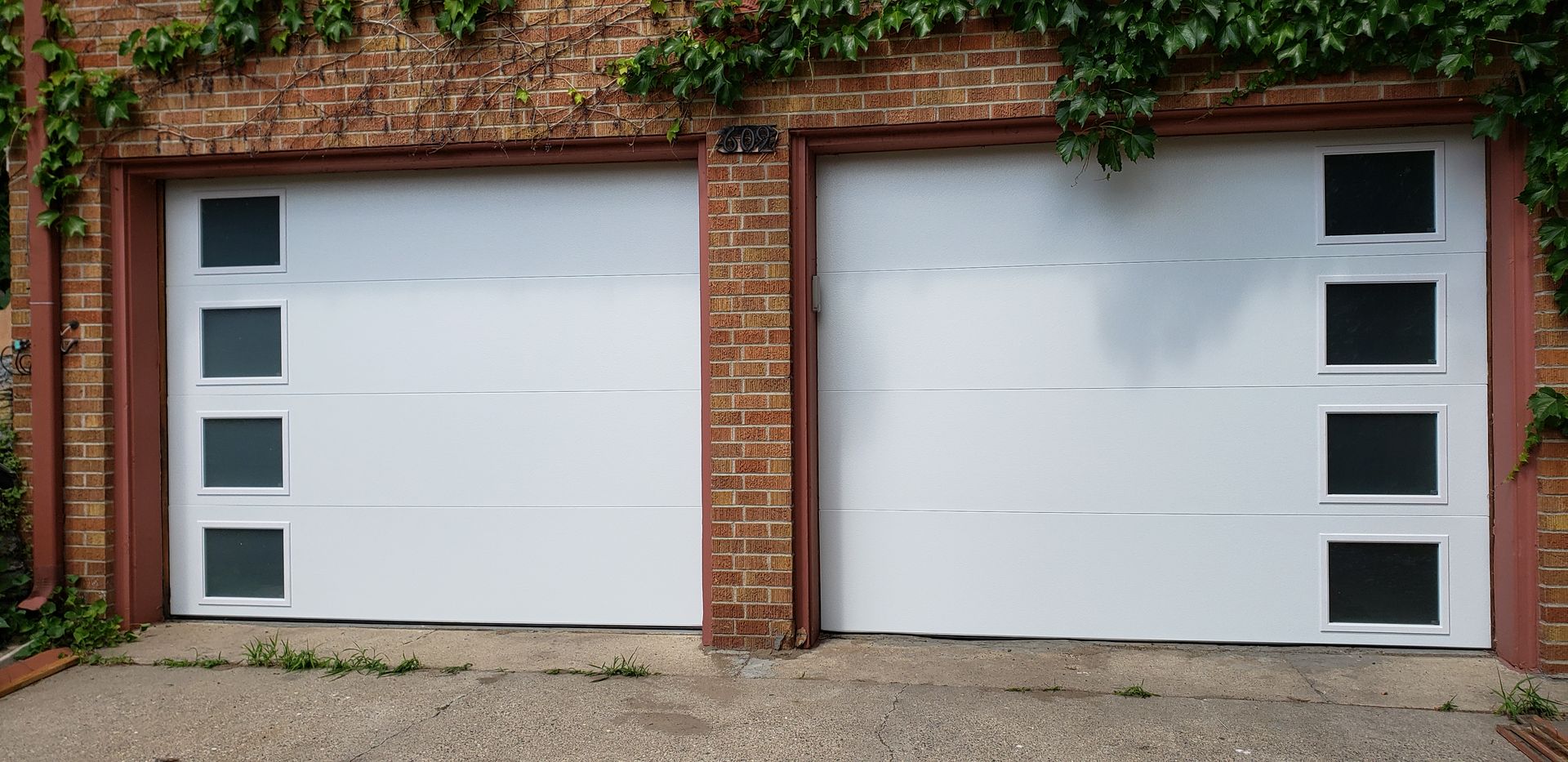 Two white garage doors set in a brick wall with ivy around the edges