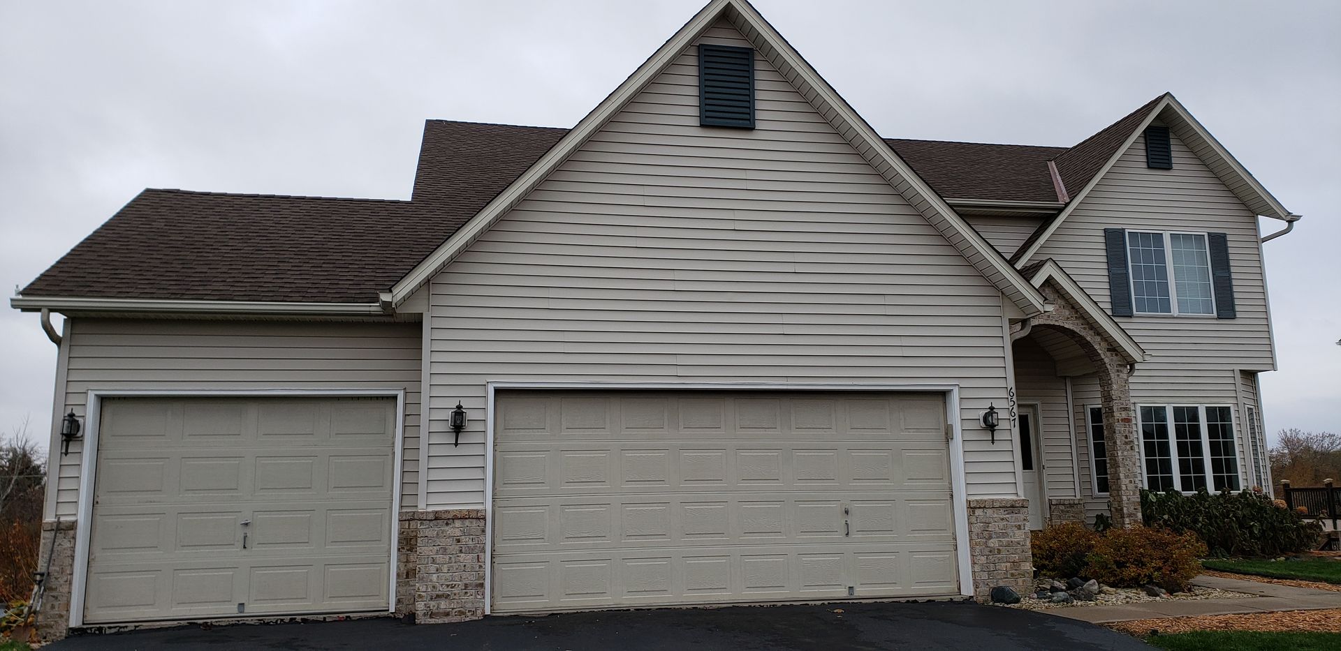 Suburban house exterior with three garage doors and light gray siding