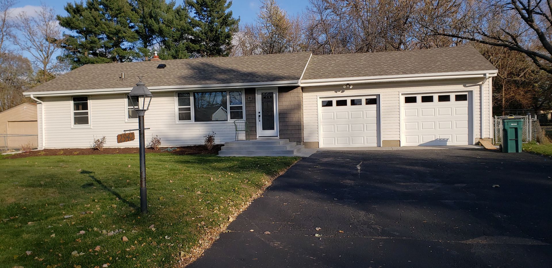 Single-story suburban house with a two-car garage, black driveway, and front lawn in daylight