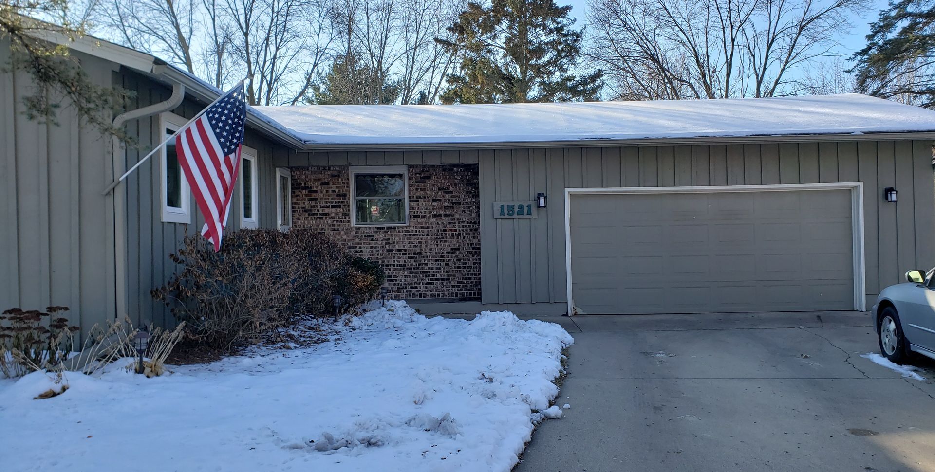 Snowy suburban house with an American flag, brick facade, and attached garage