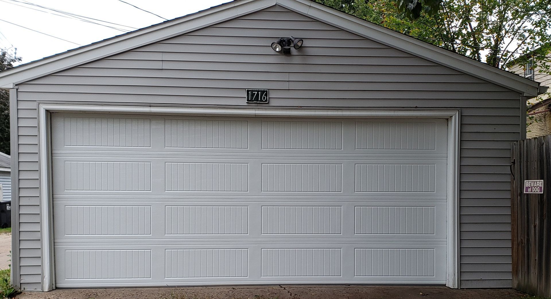 Gray two-car garage with white paneled doors and a gabled roof in a residential yard