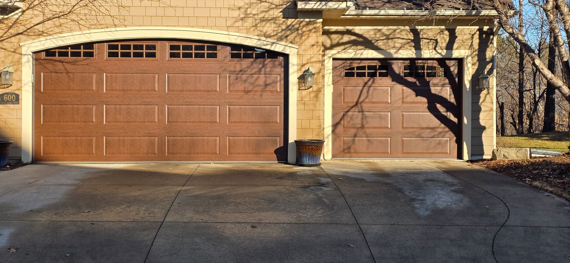 Two wooden garage doors beneath a stone archway, with a small tree and a driveway in front.