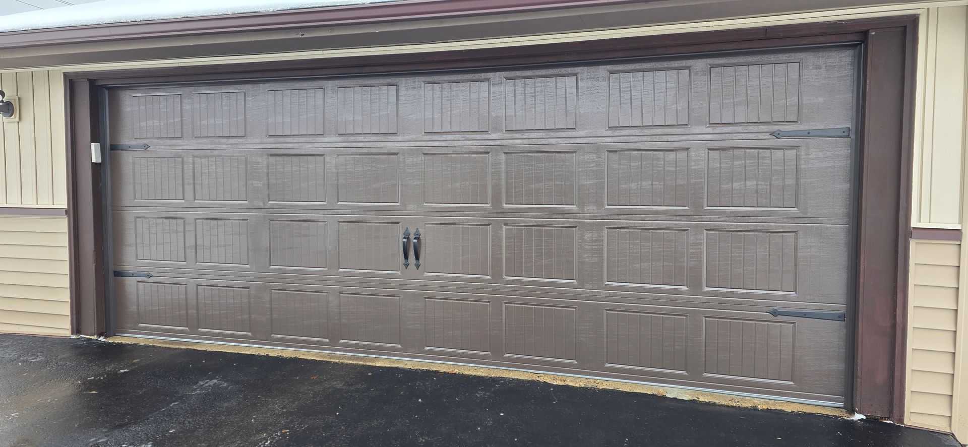 Closed brown garage door on a beige house, viewed from the driveway.