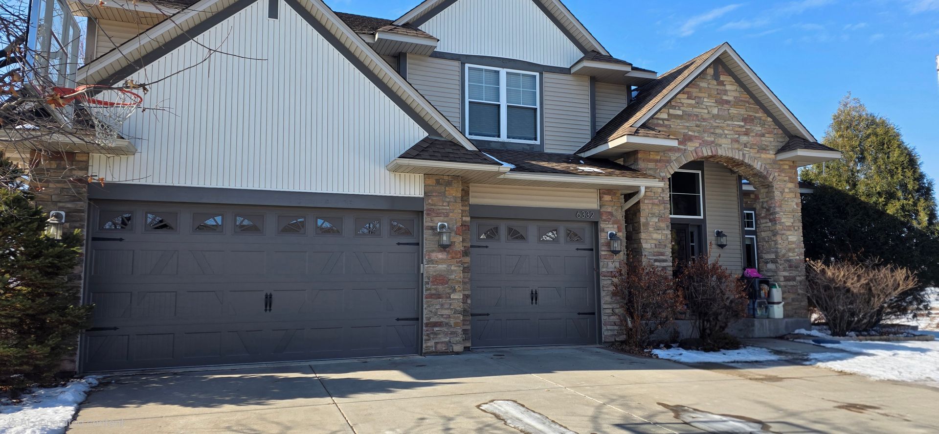 Snow-dusted suburban house with stone facade, two garage doors, and a front porch.