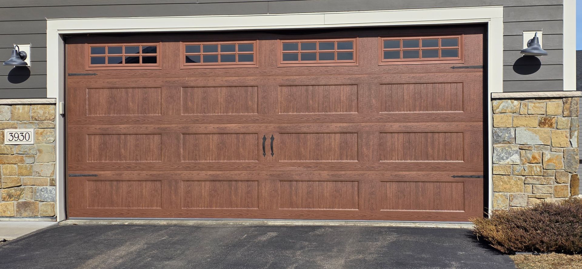 Wooden two-car garage door with small windows, set in a stone-and-stucco house exterior
