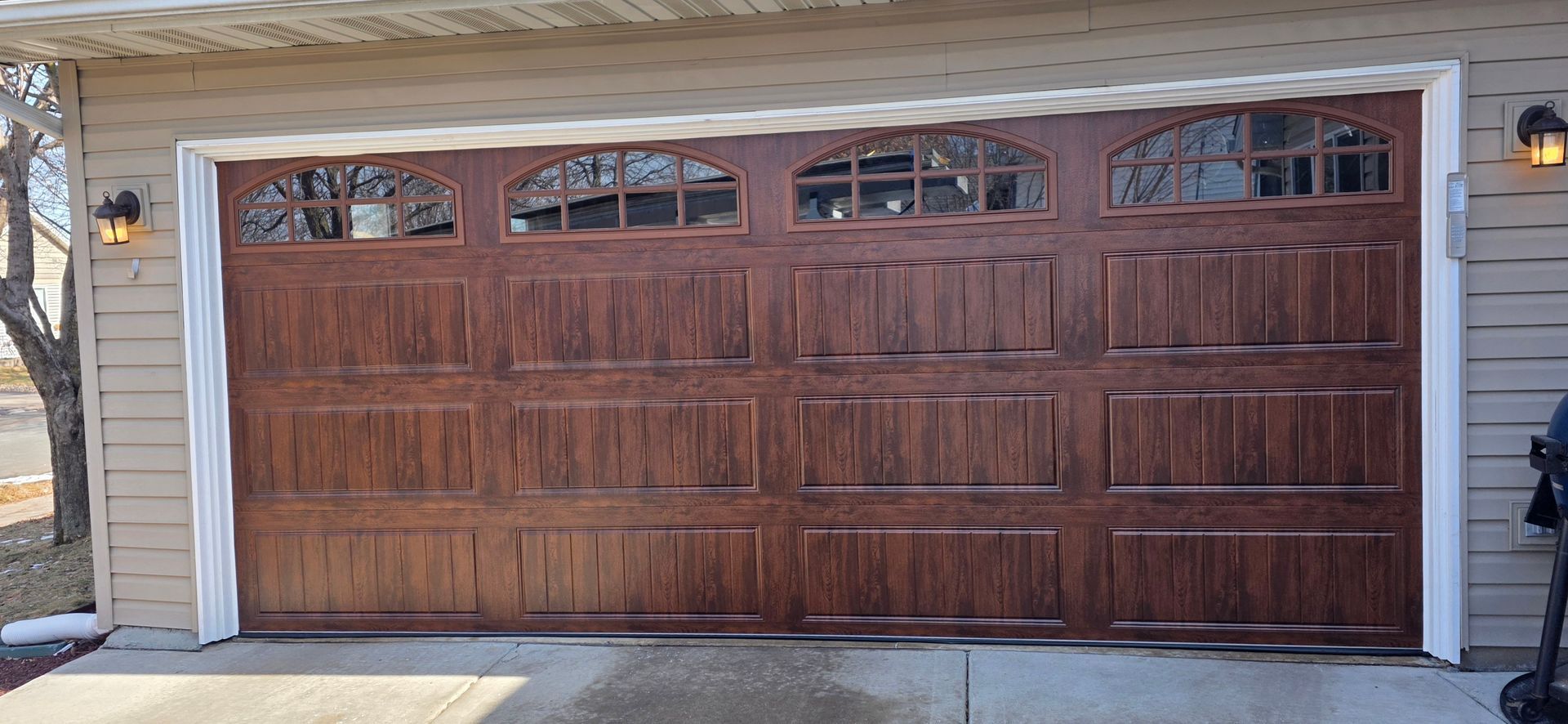 Wooden double garage door with arched windows on a house exterior, viewed in daylight.