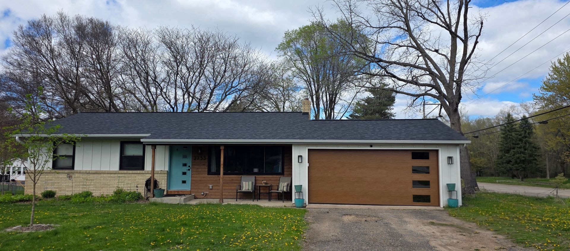 Single-story house with blue trim, wood siding, and a driveway under a cloudy sky
