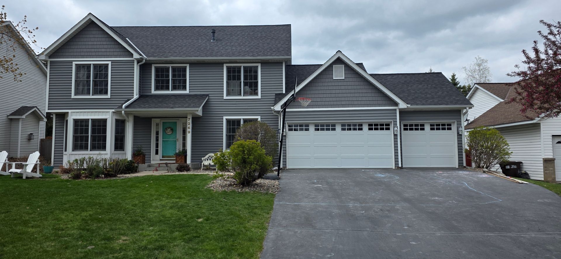 Gray two-story suburban house with white trim, attached double garage, and driveway under cloudy skies