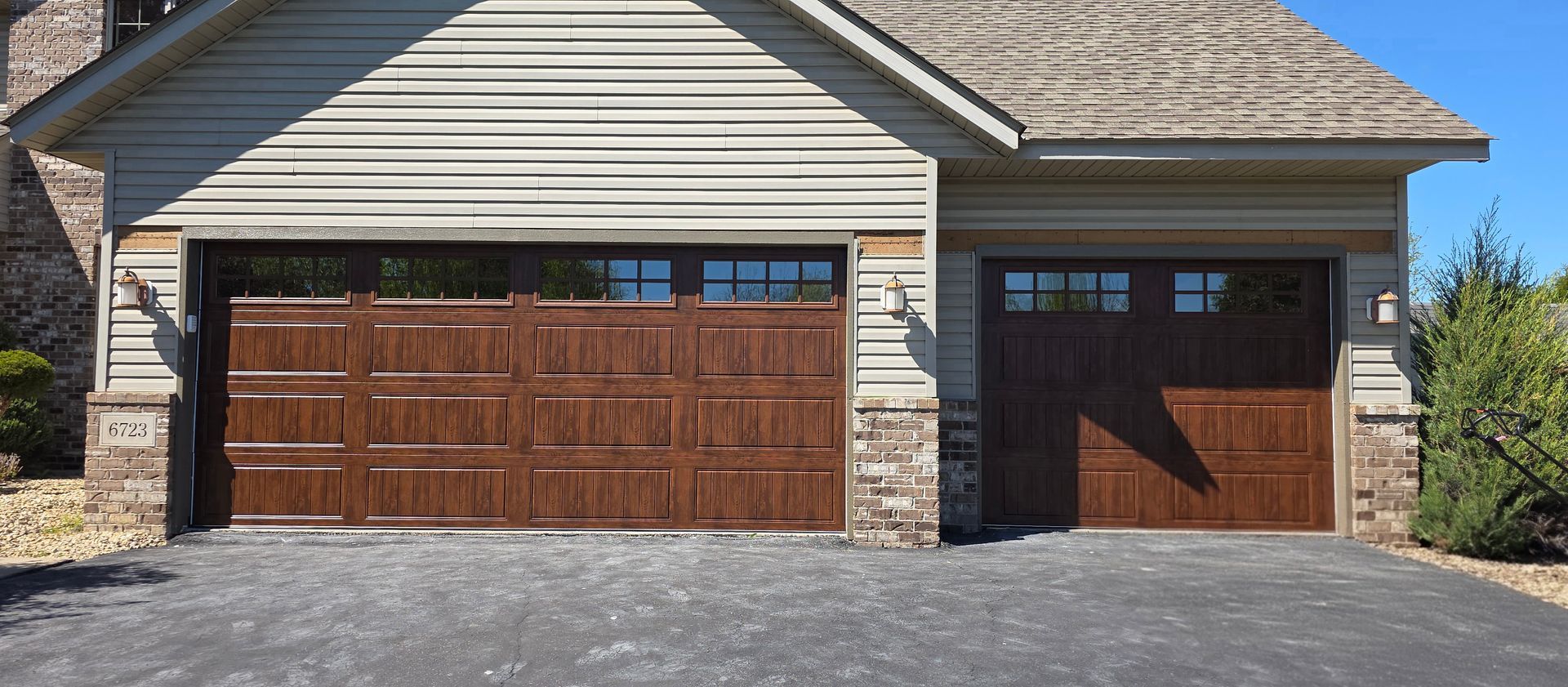 Two brown garage doors on a gray stone house exterior with a driveway in front