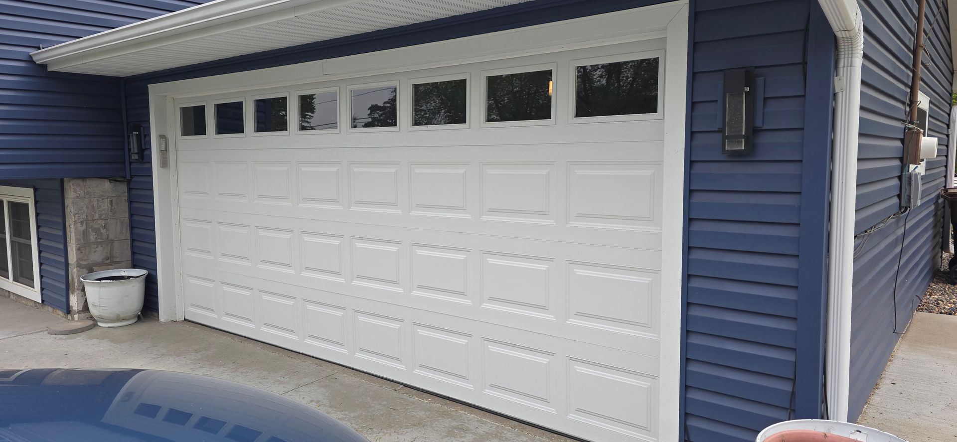 Black paneled garage door with small windows and a patterned lower section on a house exterior