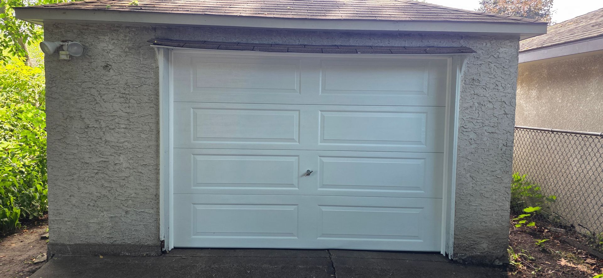 White double garage door on a small stucco outbuilding with a low shingled roof.