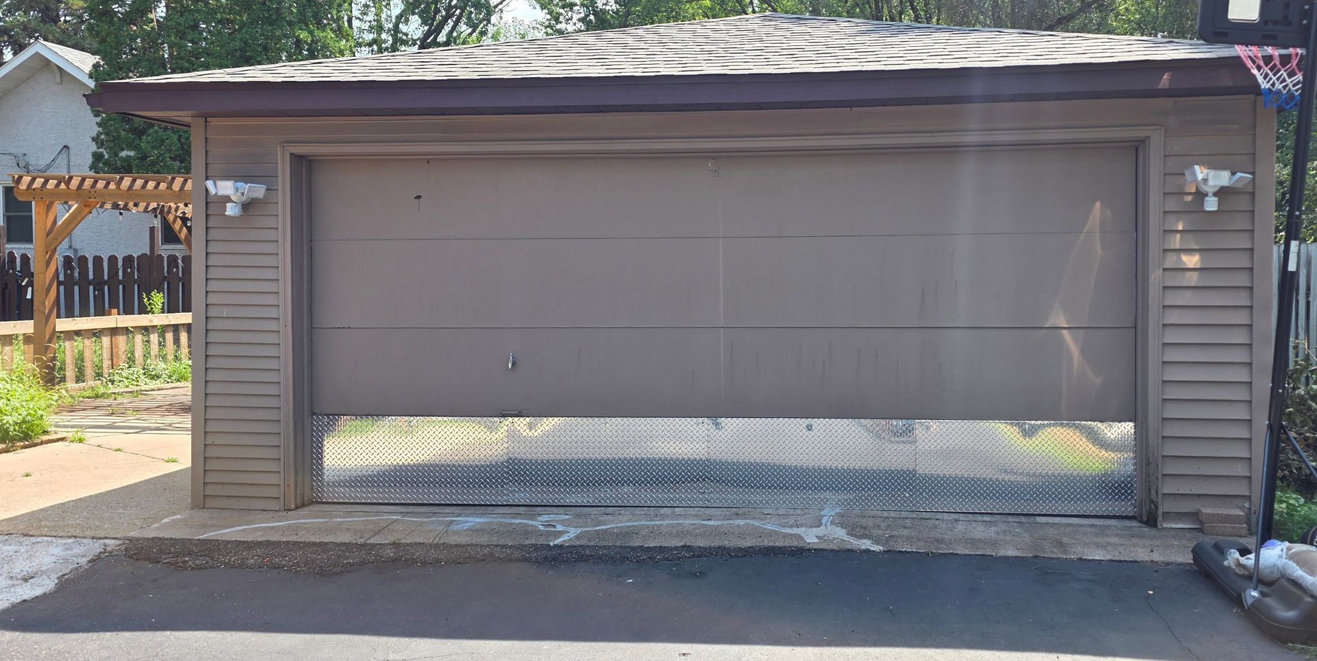 Gray detached garage with a closed roll-up door and a white crossbuck gate in front