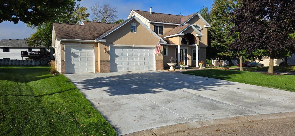 Suburban house with a large concrete driveway and green lawn on a sunny day
