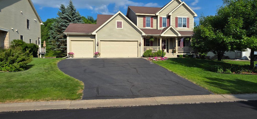 Suburban house with a black driveway, beige garage, and green lawn on a sunny day