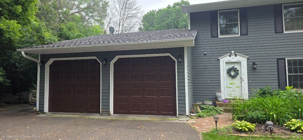 Gray suburban house with a double garage, white trim, and a front door beside landscaped shrubs