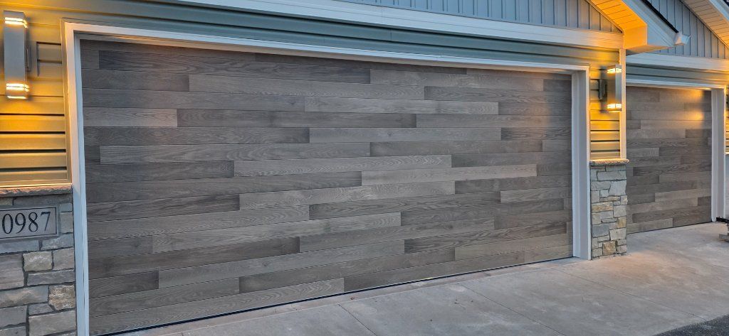 Modern house garage with gray wood-paneled doors and warm exterior lights at dusk