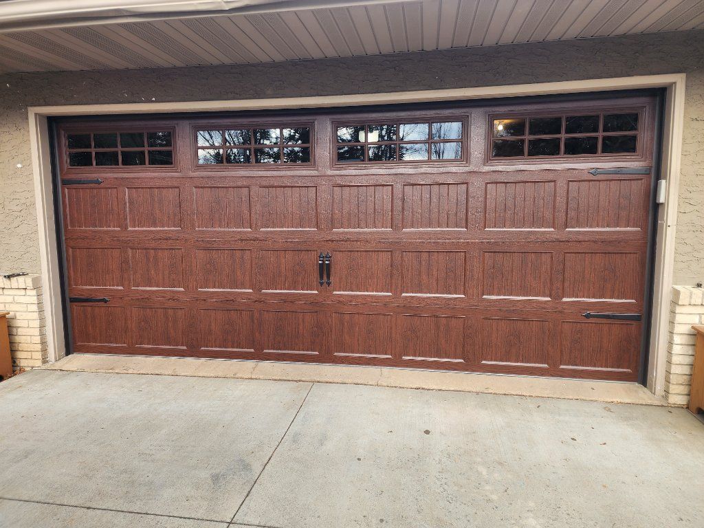 Brown double garage door with upper windows under a covered driveway.