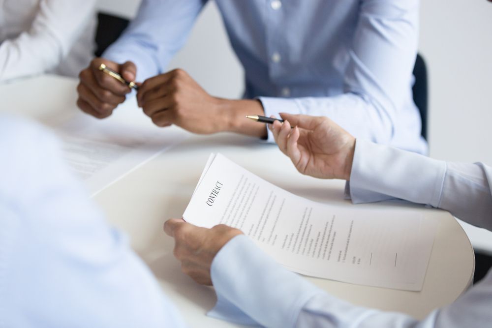 A Group Of People Are Sitting At A Table Signing A Contract — Queensland Lawyers Cairns In Cairns City, QLD
