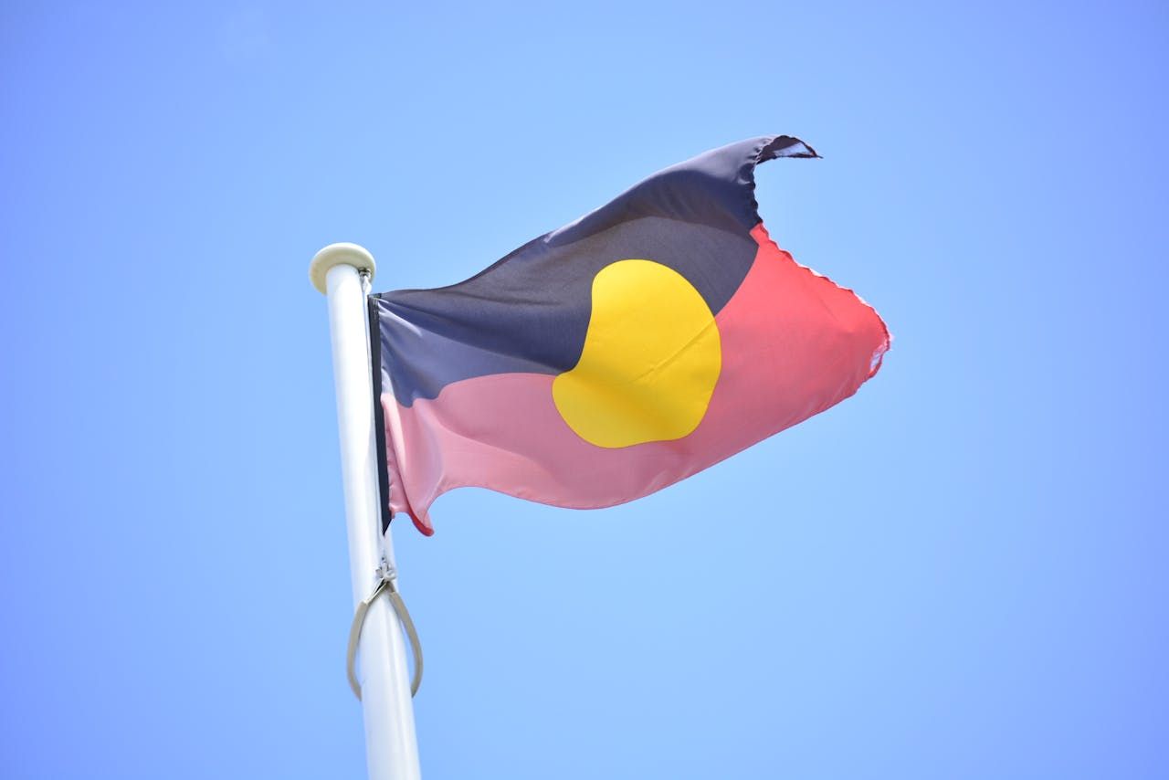 An aboriginal flag is flying in the wind against a blue sky