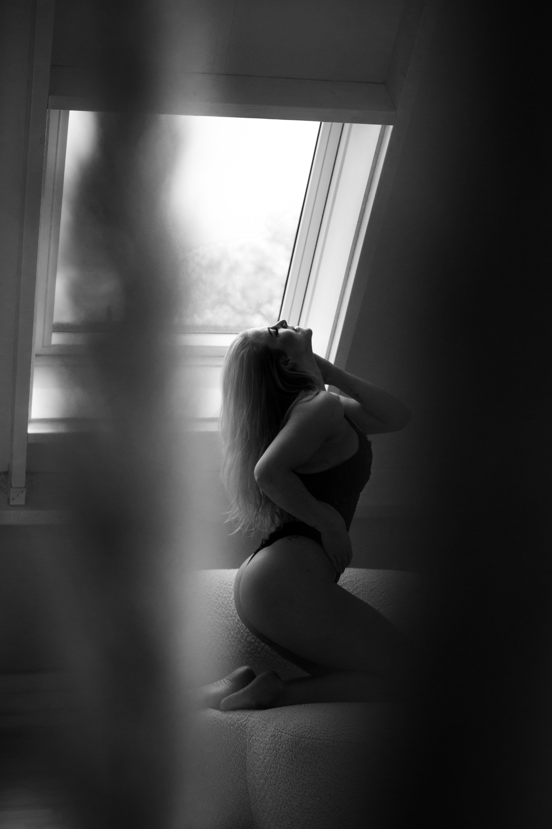 Een vrouw knielt en kijkt omhoog bij een raam. Zwart-witfoto, onscherp met een wazige voorgrond.