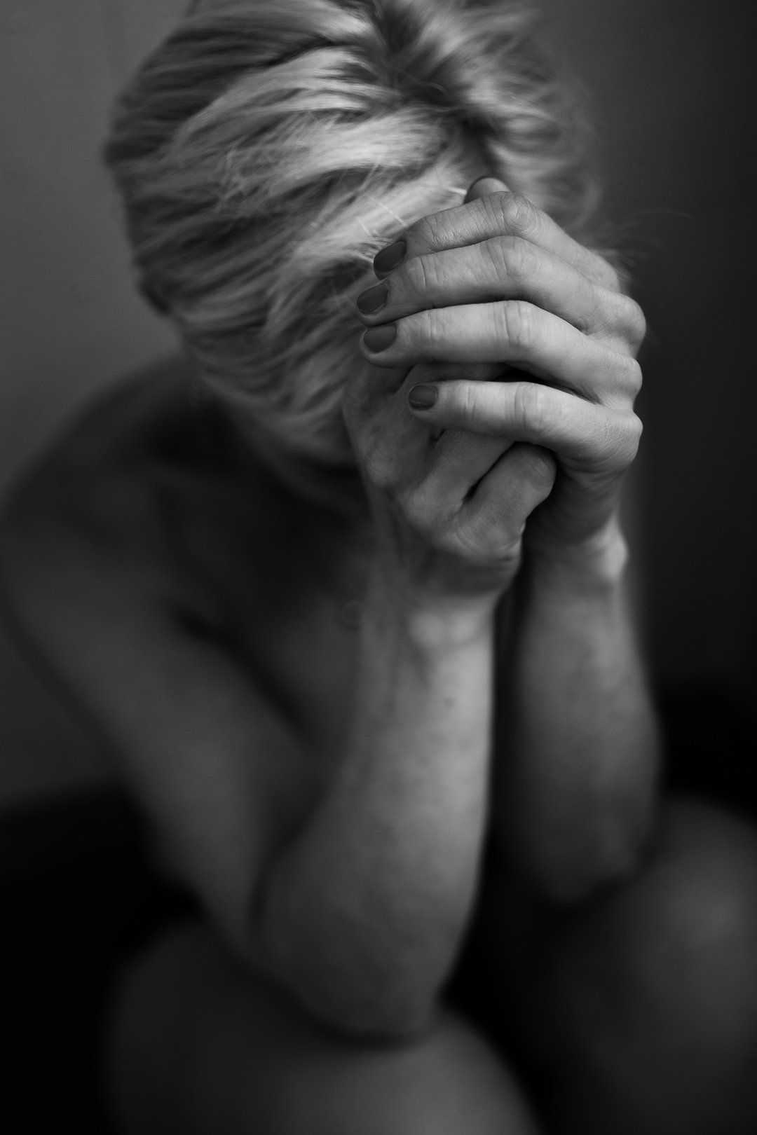 Vrouw, handen ineengevouwen, gezicht verborgen. Zwart-wit.