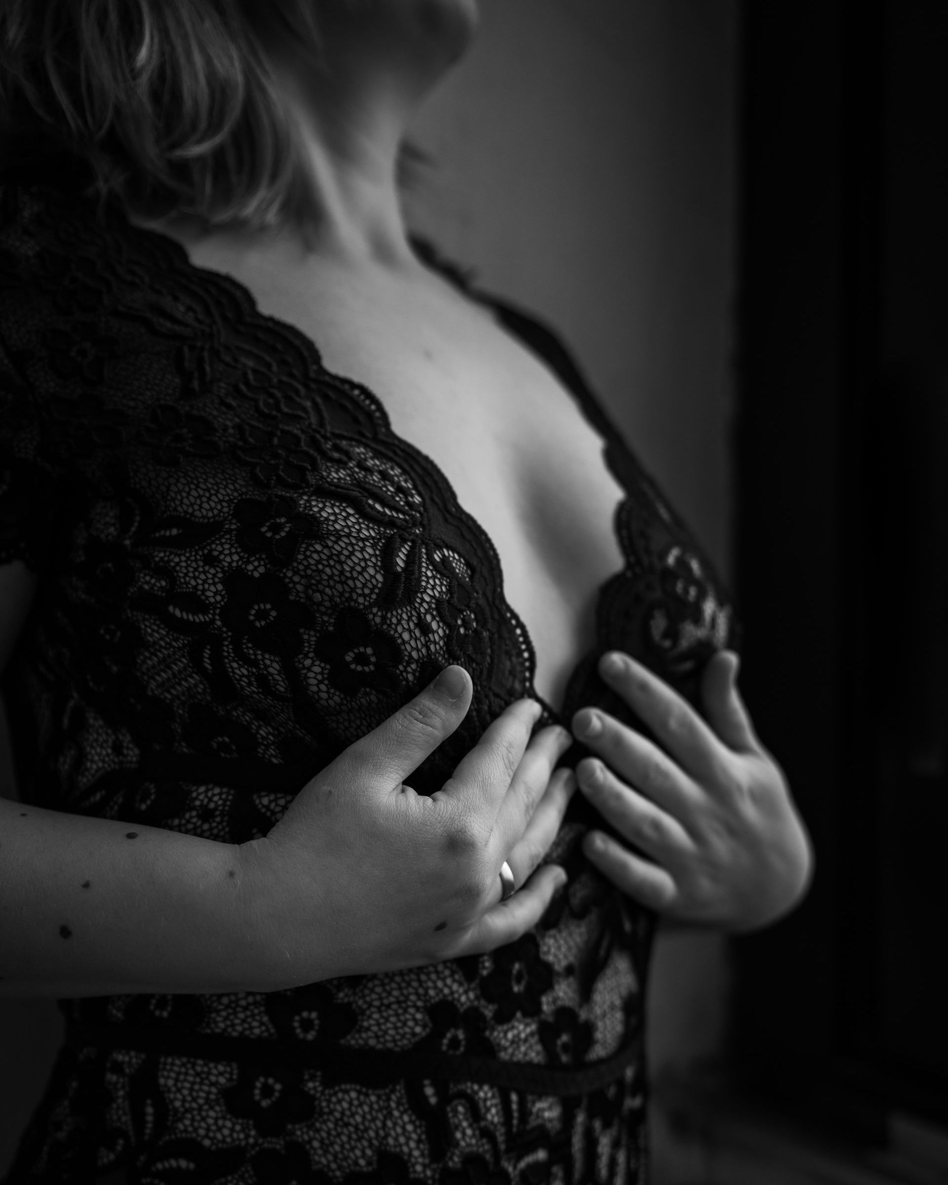 Vrouw in zwarte kanten lingerie, handen op de borst, binnen.