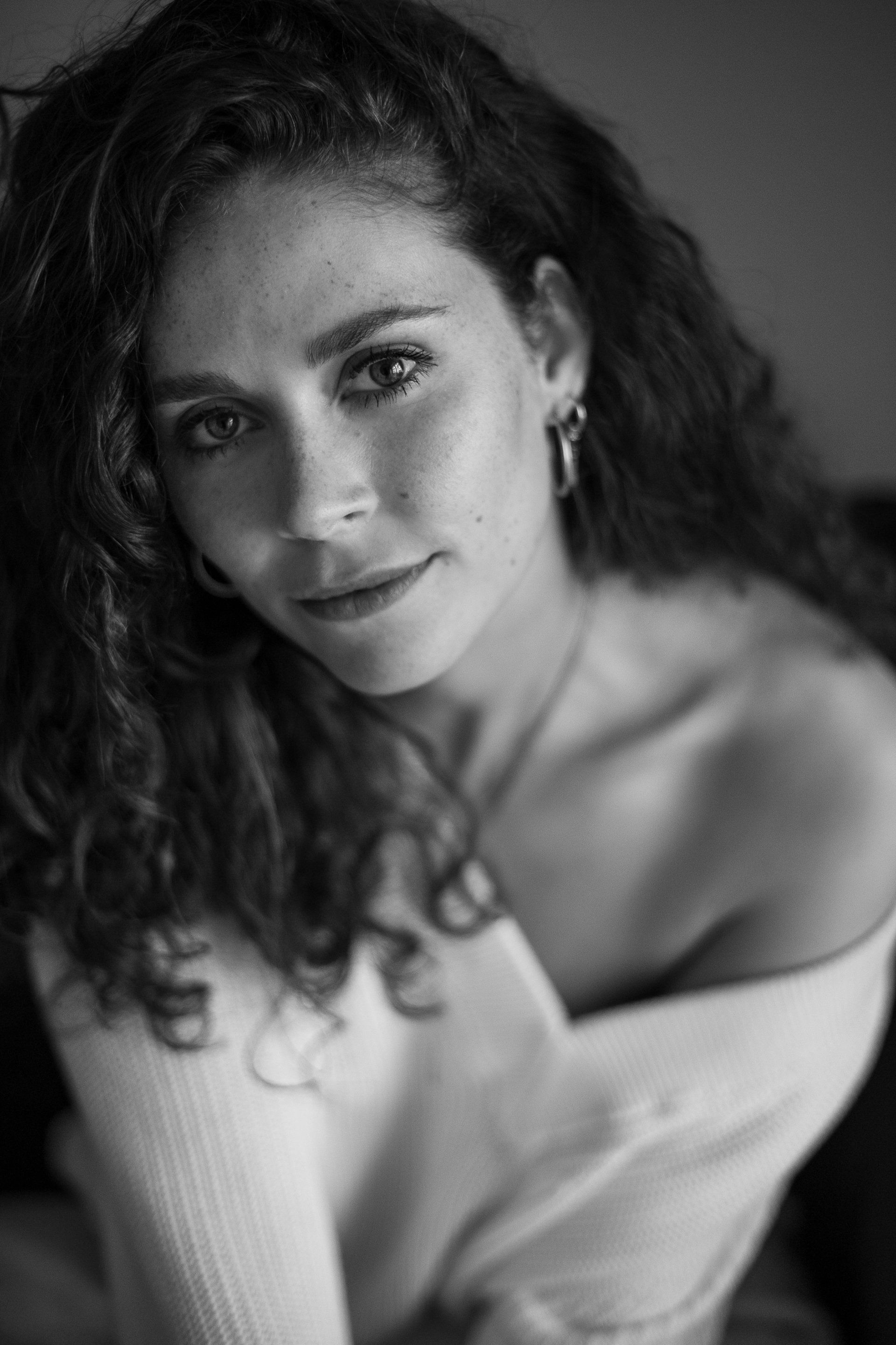 Vrouw met krullend haar kijkt in de camera, gekleed in een trui, in zwart-wit.