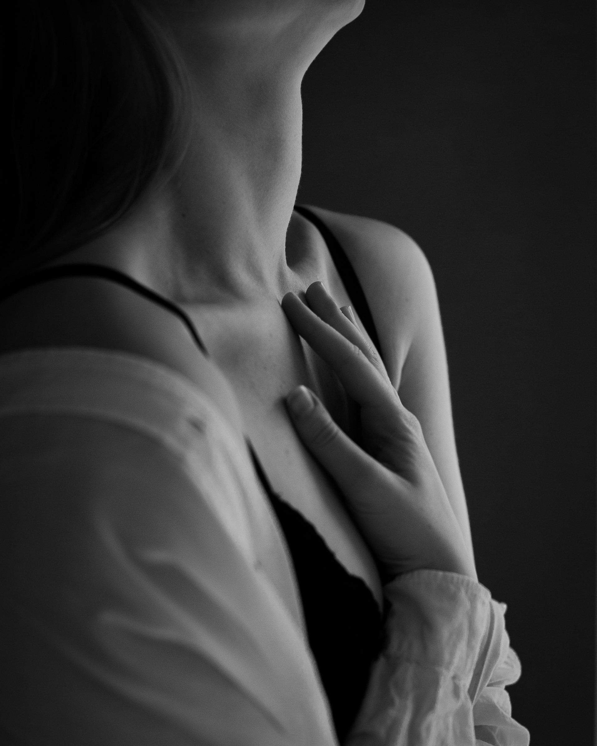 Vrouw in zwarte bh en open wit shirt, hand op de borst, kijkt omhoog.