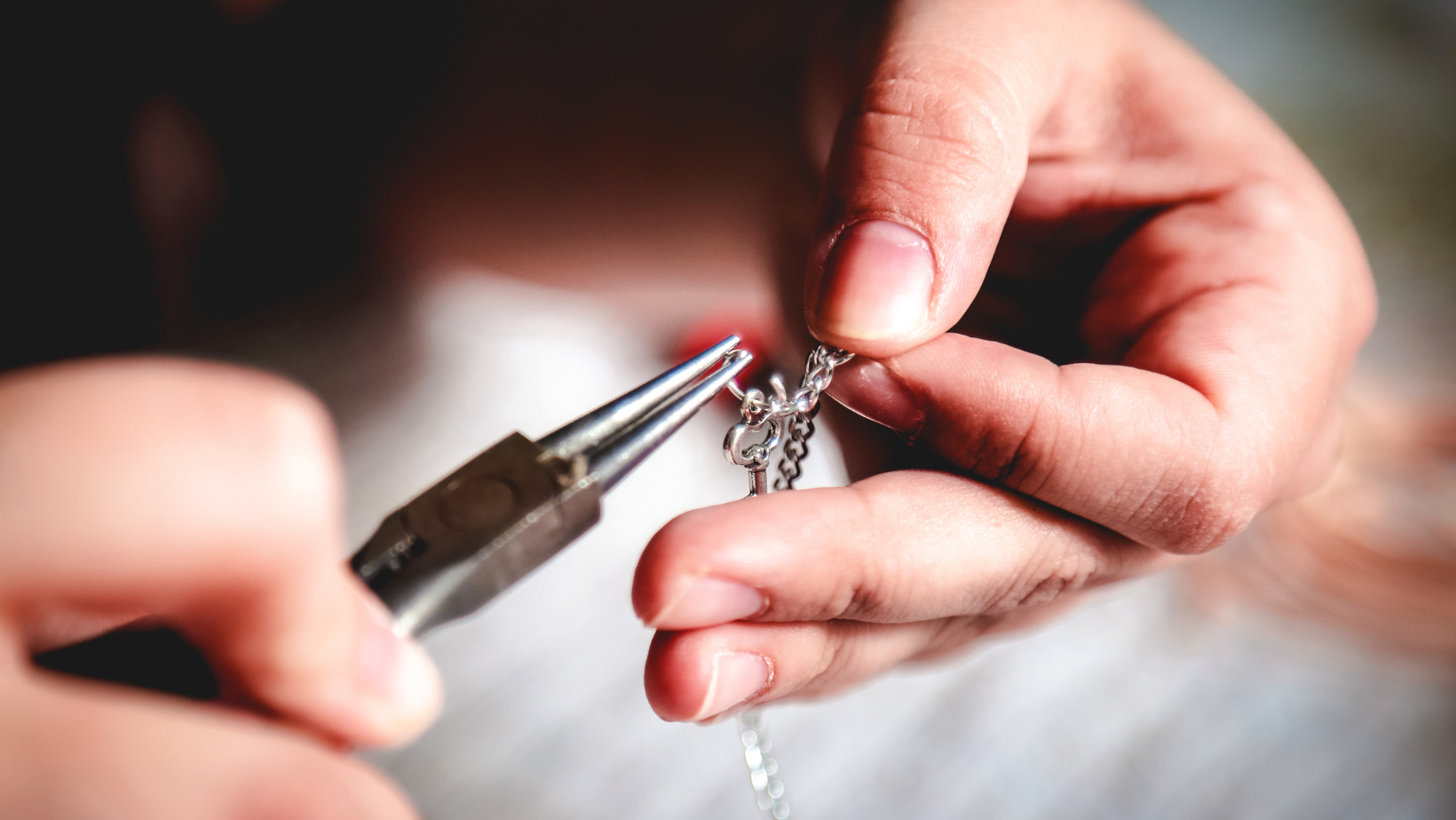 Hands using pliers to repair a silver necklace.