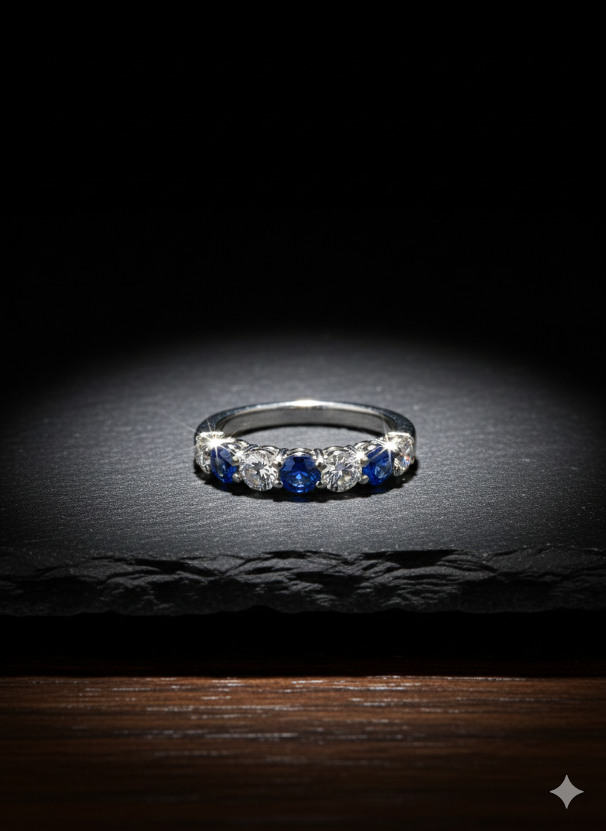 Diamond and sapphire band ring on a dark surface, lit from above.
