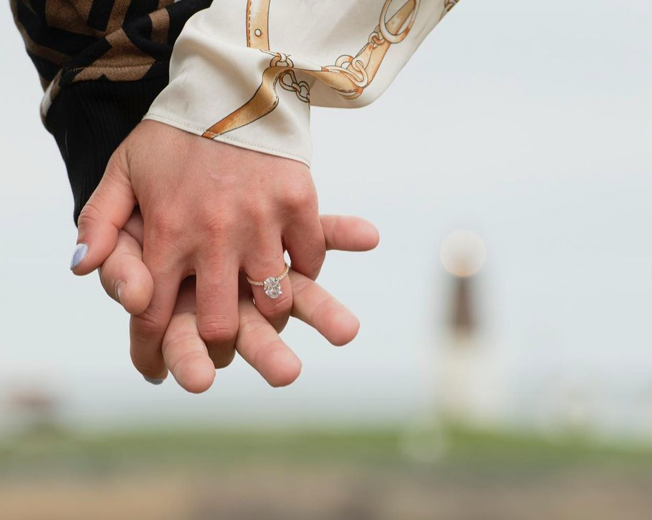 Hands clasped, engagement ring visible, outdoors.