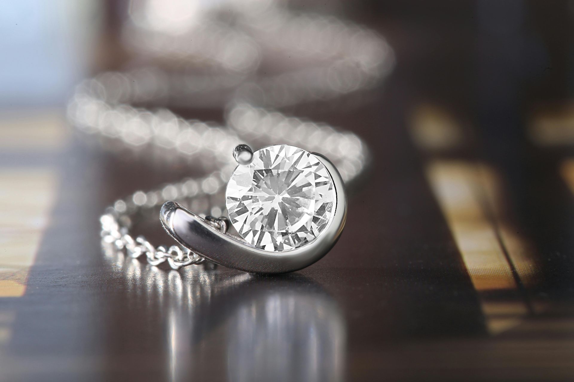Diamond pendant necklace on a reflective surface, close-up with a blurred background.
