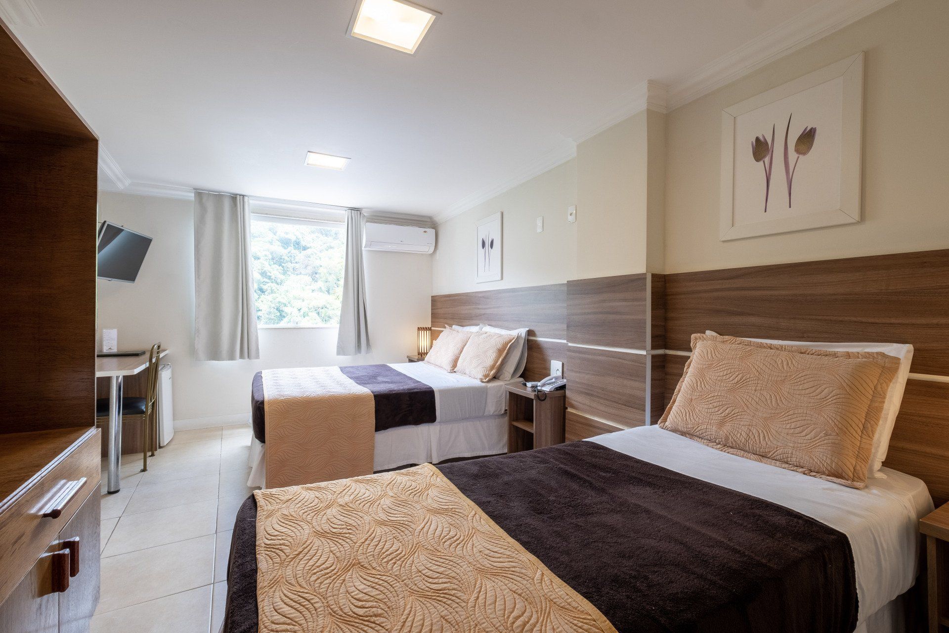 Quarto de hotel com duas camas, tons neutros, detalhes em madeira e uma janela.