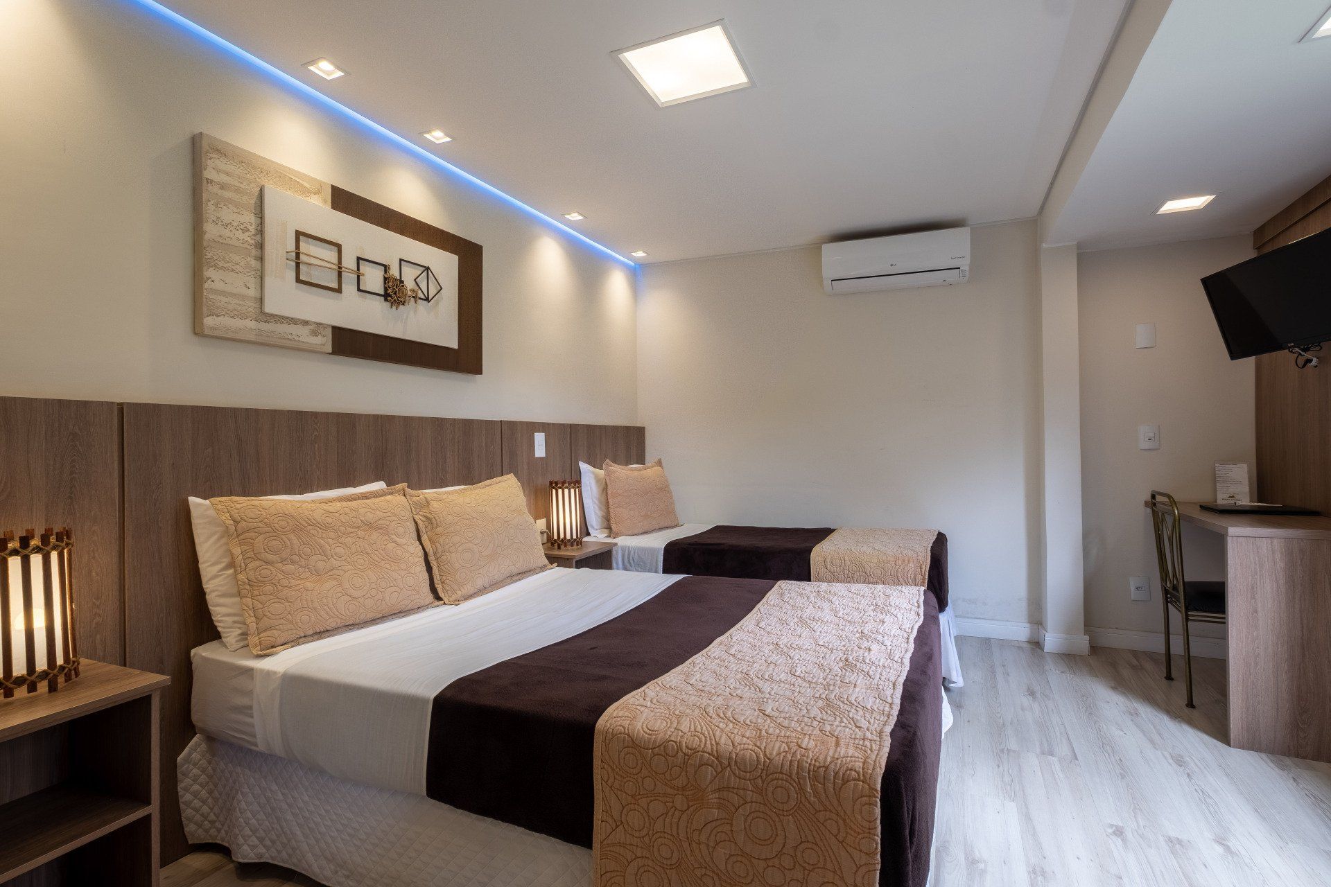 Quarto de hotel com uma cama de casal e uma de solteiro, tons neutros e decoração moderna.