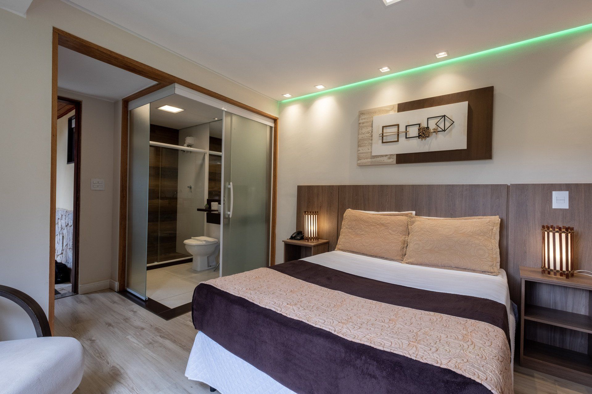 Quarto com cama queen-size, banheiro privativo, tons neutros, detalhes em madeira e iluminação decorativa.