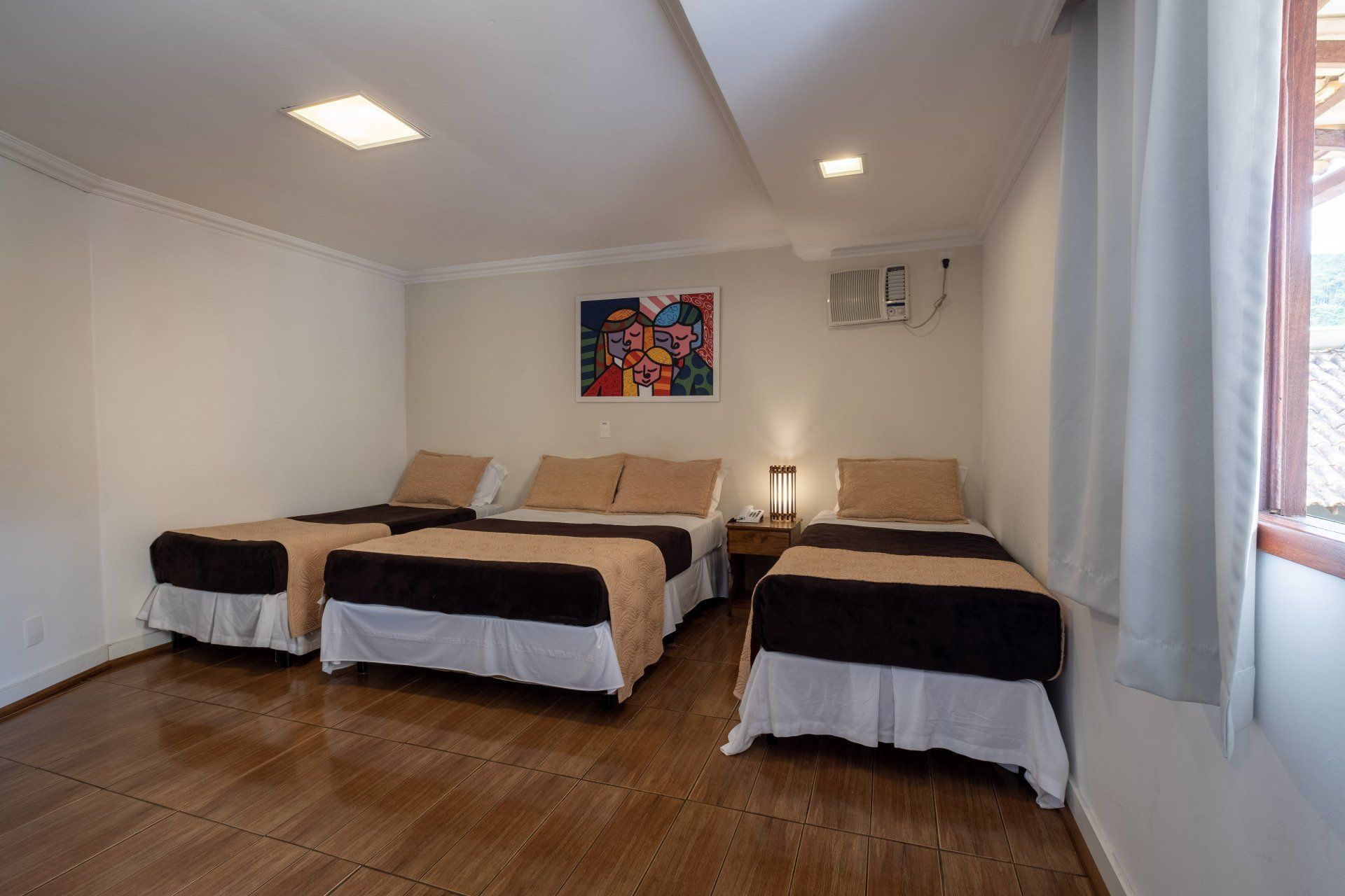 Um quarto de hotel com três camas de solteiro, paredes brancas e uma pintura abstrata colorida.