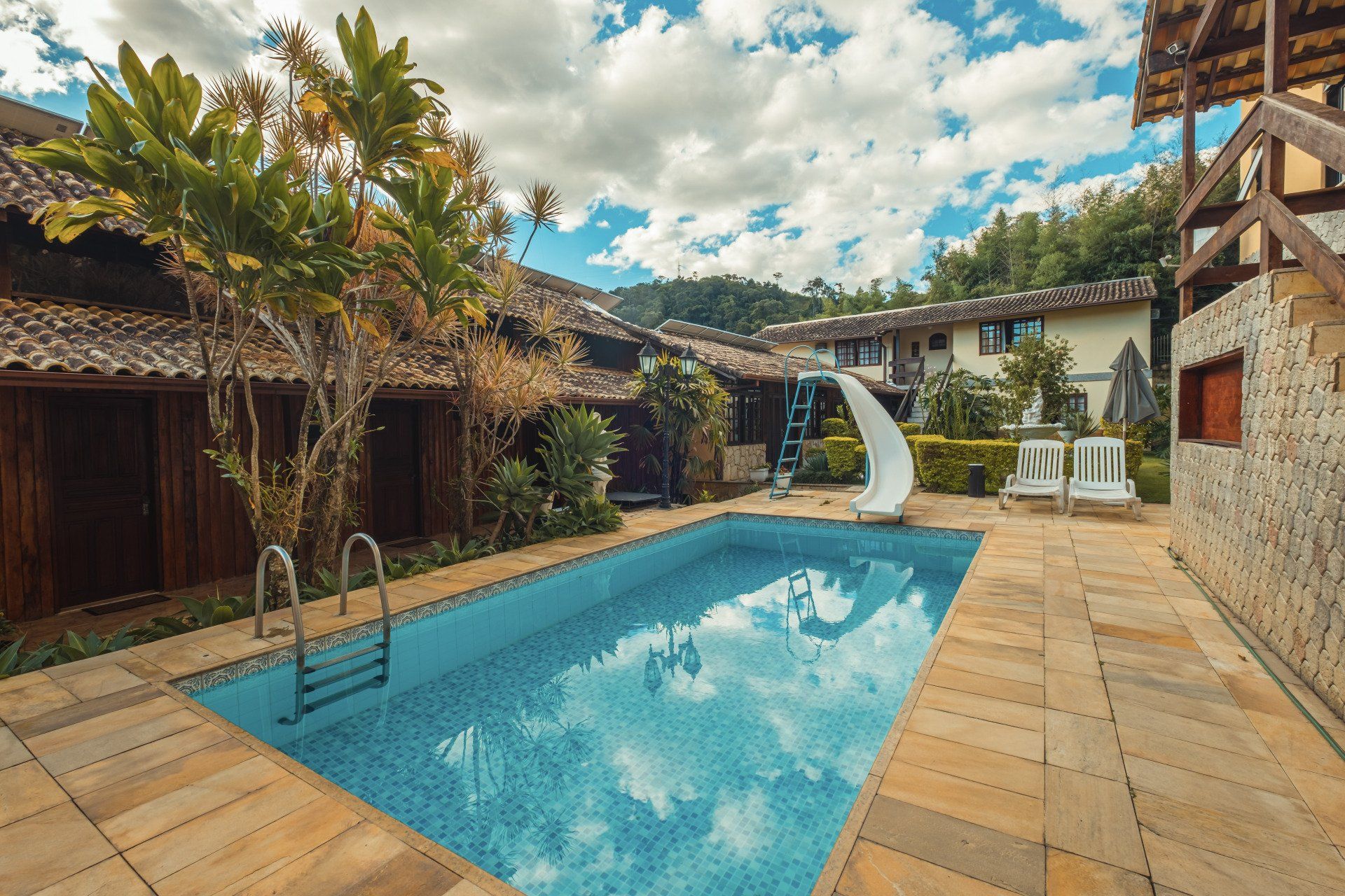 Piscina em um pátio, cercada por prédios, com um toboágua, árvores e céu nublado.
