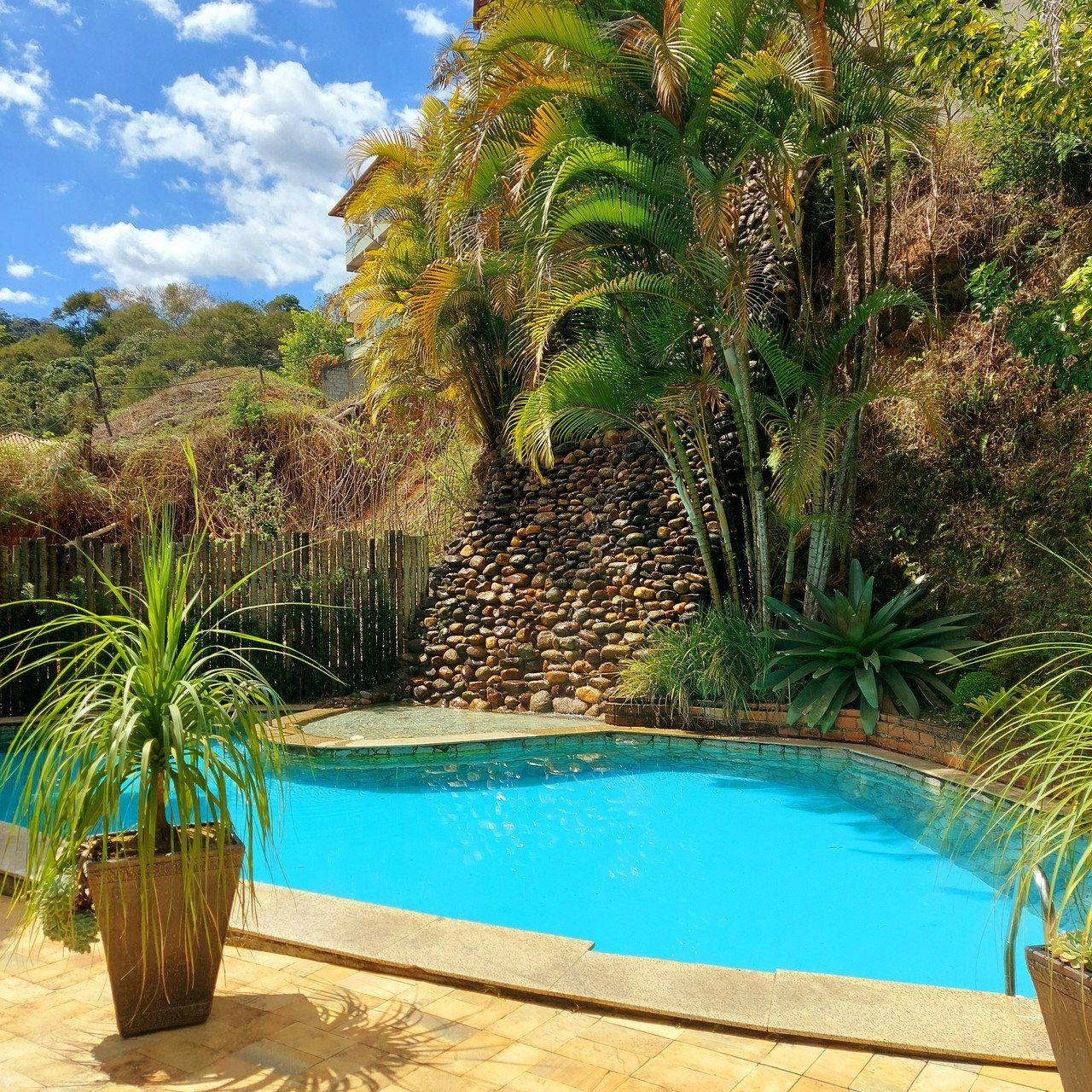 Piscina rodeada por plantas tropicais sob um céu azul nublado.