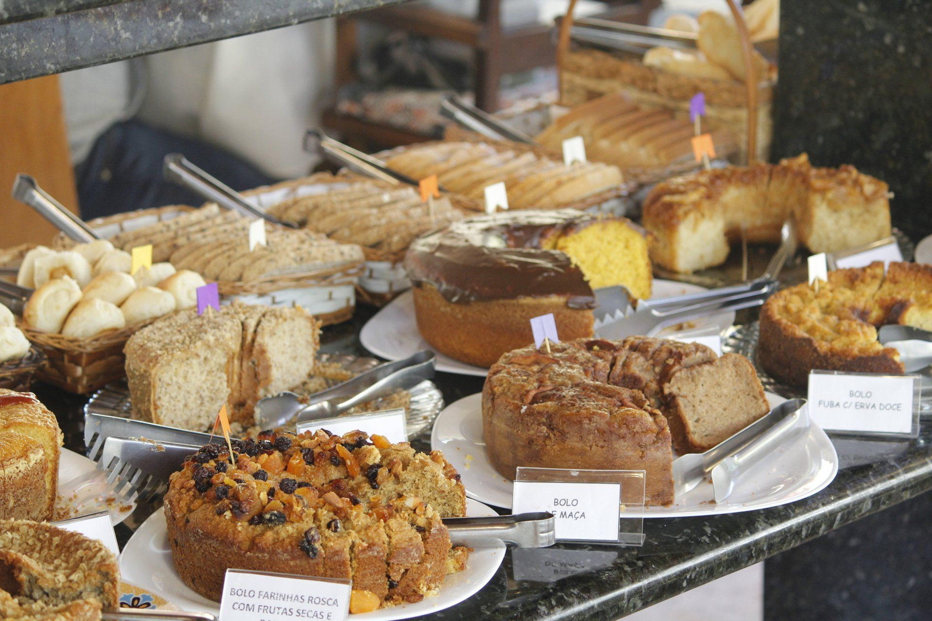 Exposição de diversos bolos e produtos de confeitaria em pratos, prontos para venda.