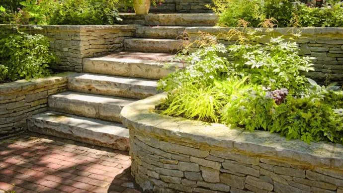 a brick walkway leading to stone stairs with some bushes