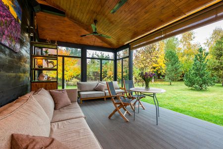 A porch with a couch , table and chairs and a ceiling fan.