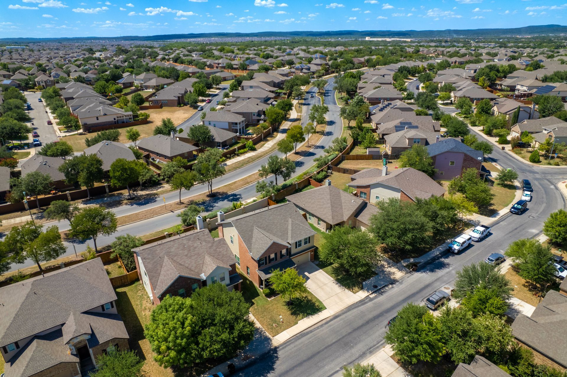 Aerial view of a suburban neighborhood with curving streets, rows of houses, and trees under a blue sky