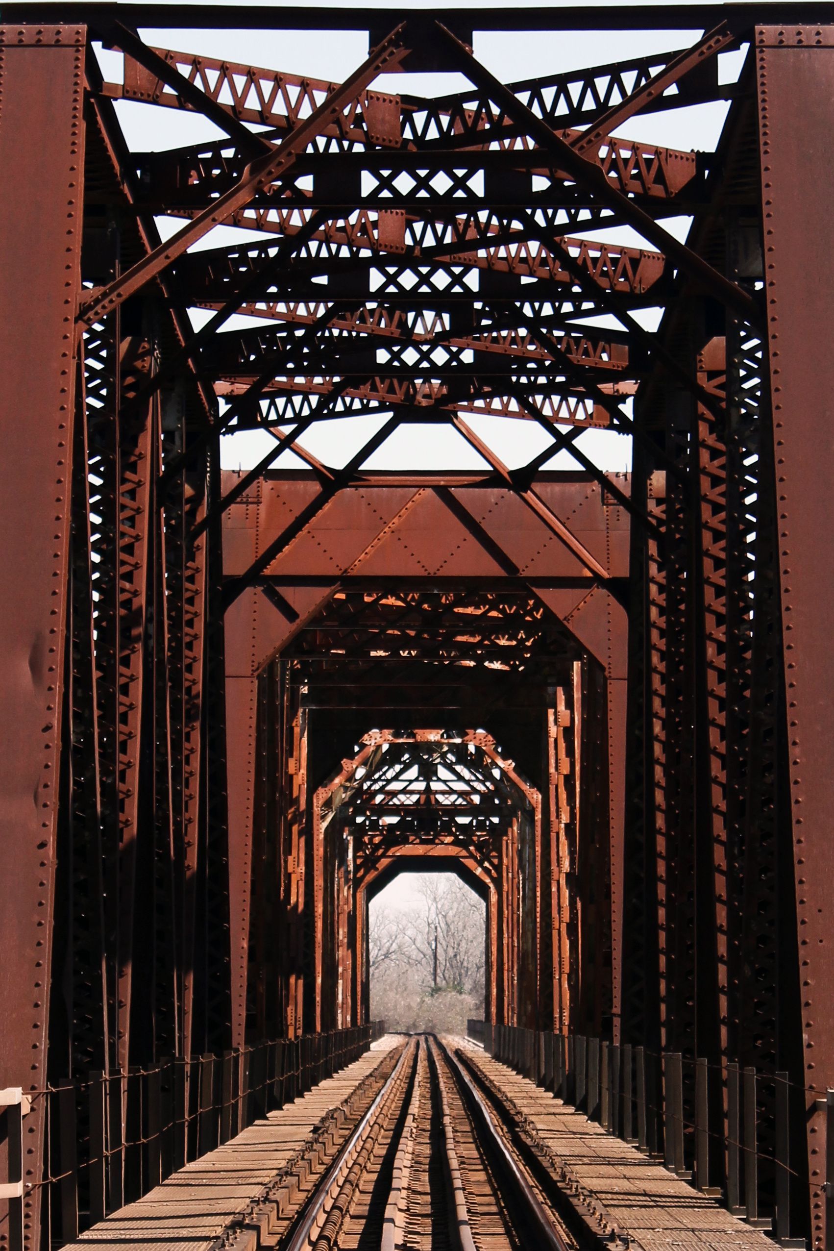 Rusty steel railway bridge with tracks leading through repeating arches into the distance