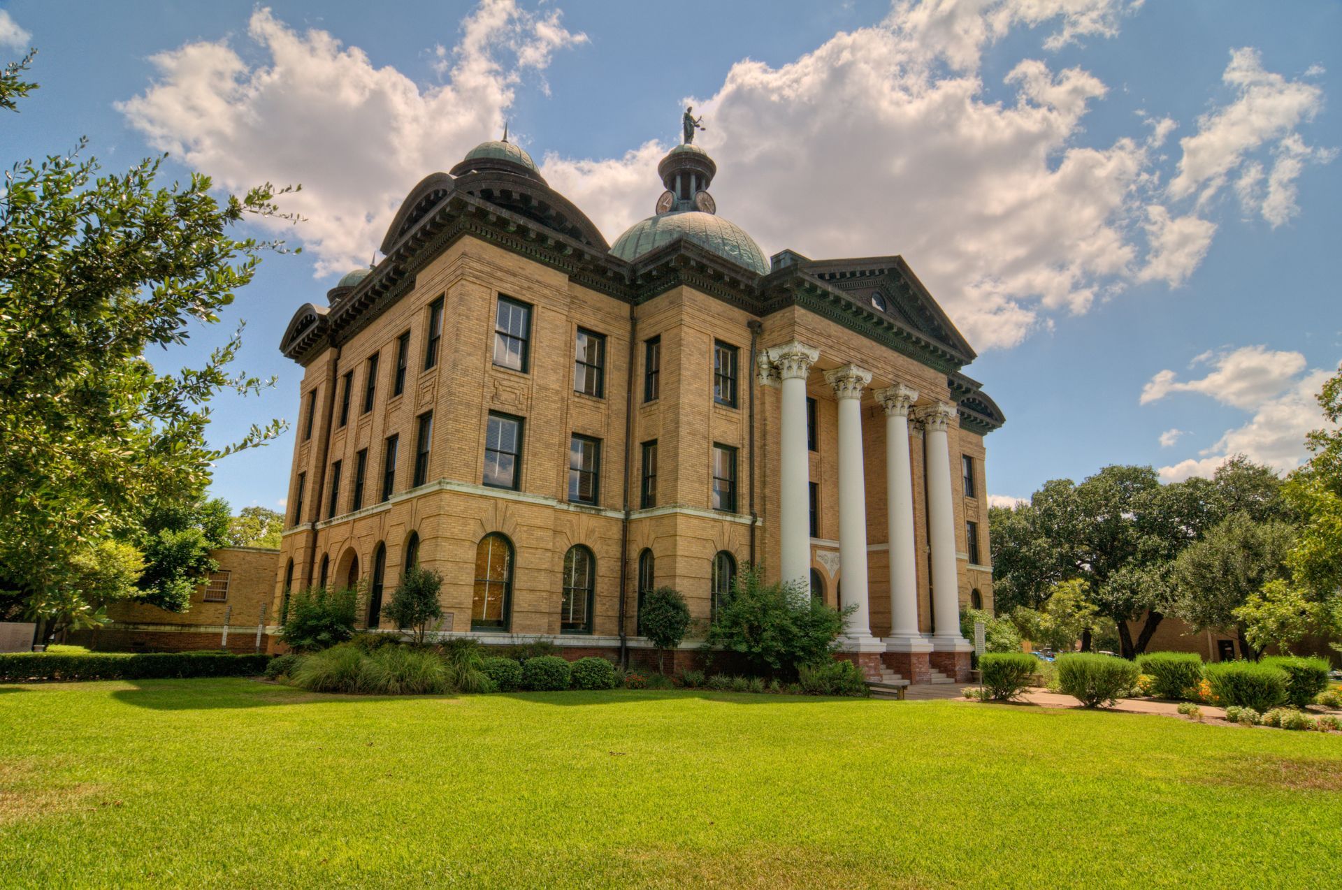 Historic brick courthouse with white columns and dome, set on a green lawn under a blue sky