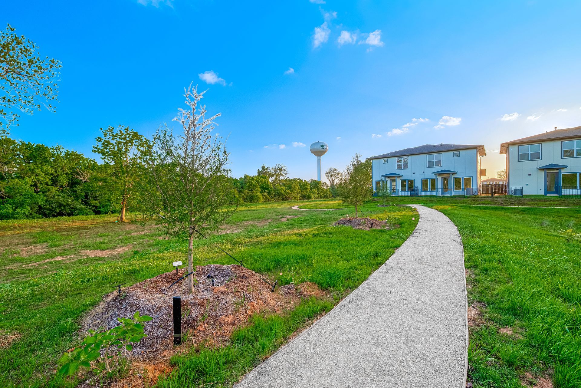 Curved gravel path through green grass toward white houses under a blue sky