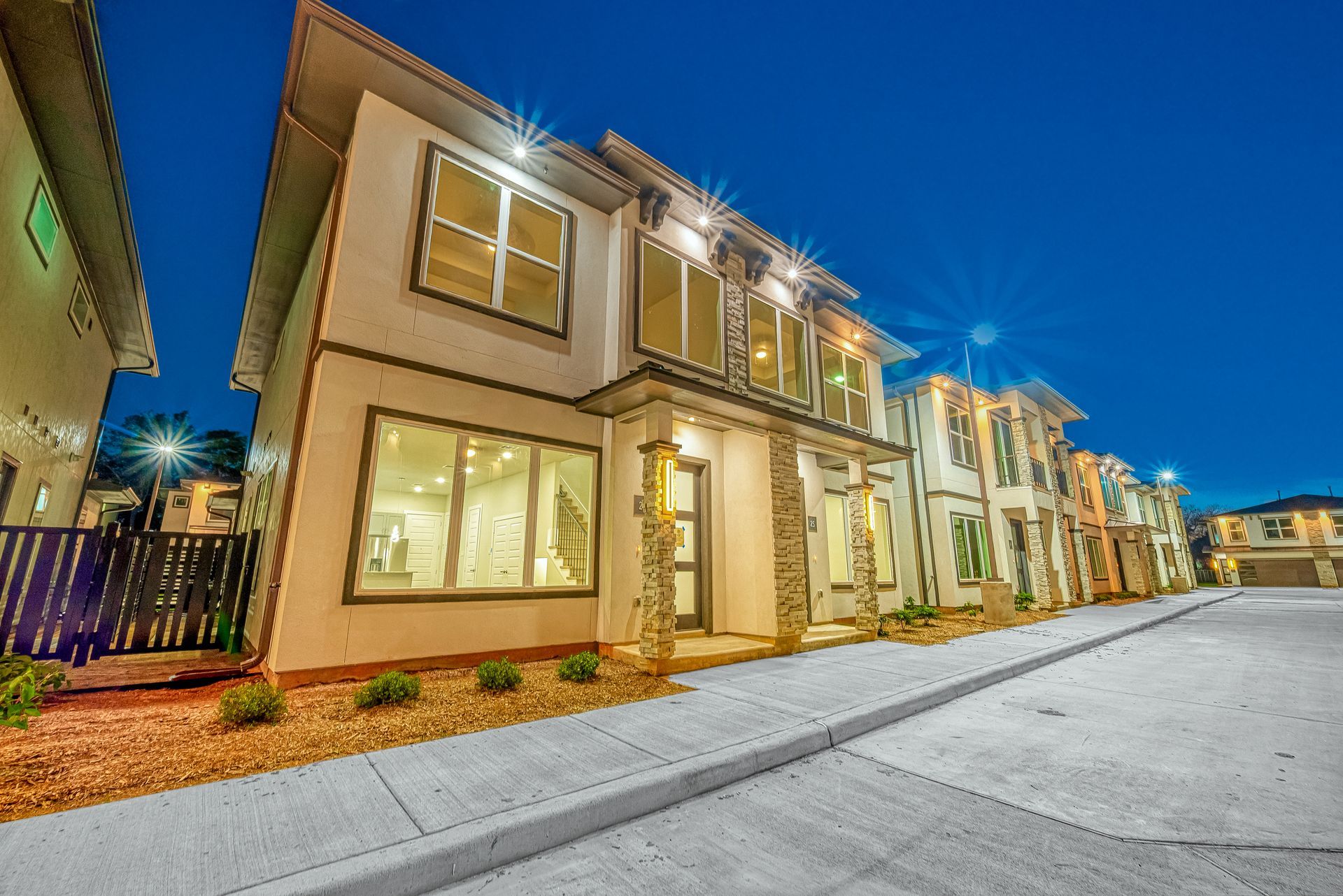 Modern two-story townhomes at dusk with lit windows and a paved street in front