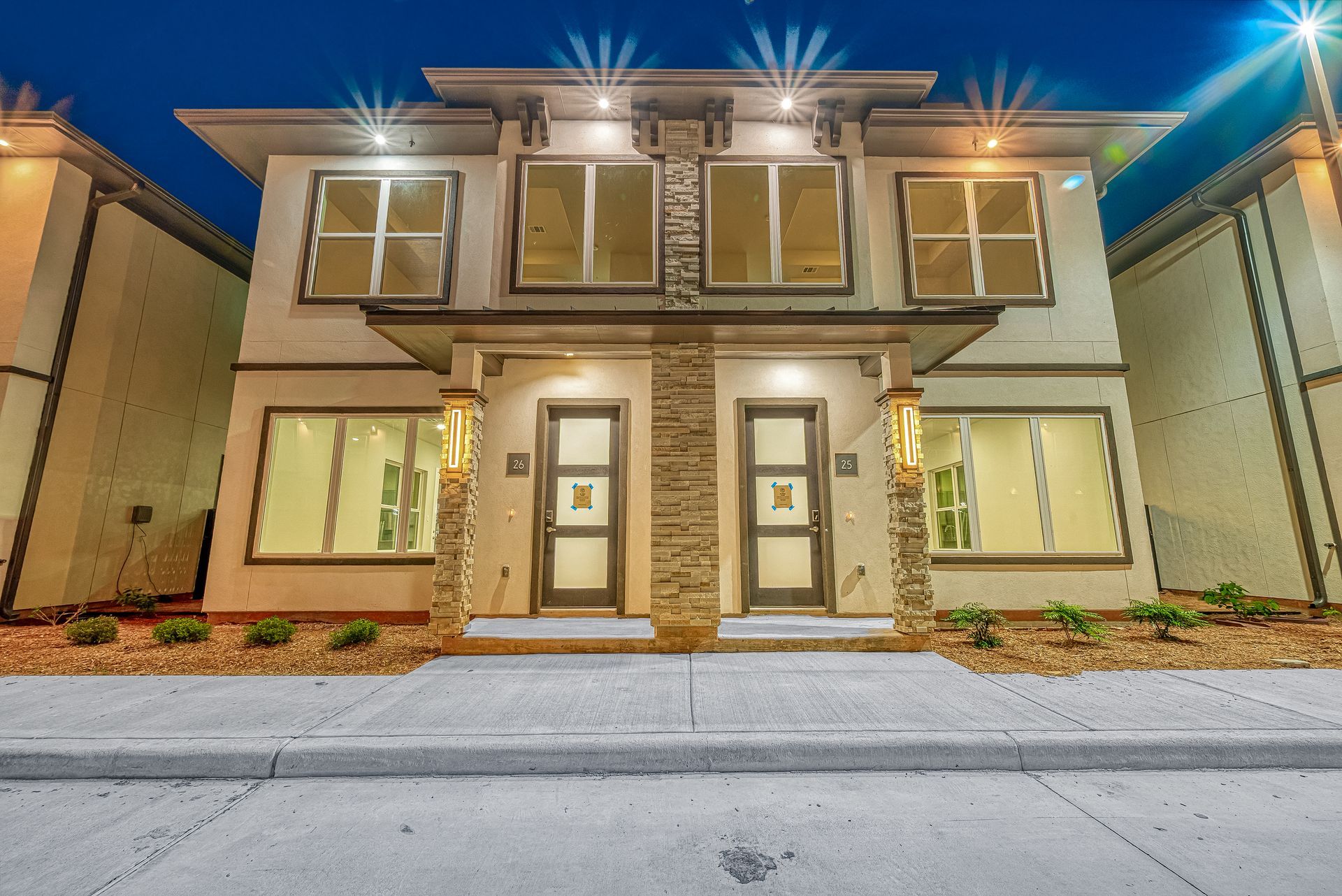 Modern two-story townhouse facade at dusk with warm exterior lights and a front walkway